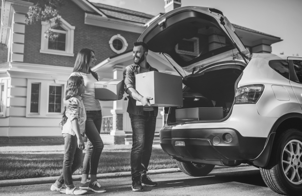 A smiling family of three loads boxes into the back of their car.