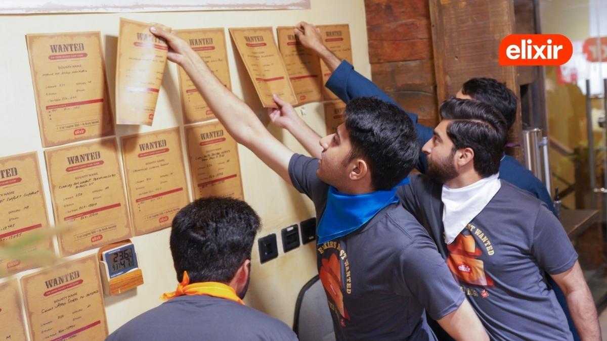 A group of Elixir Technologies employees reaches for bounty posters on a wall during Elixir's 2026 Wild West-themed hackathon.
